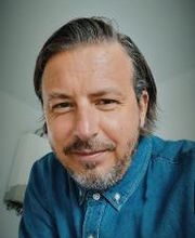 Portrait von einem Mitarbeiter mit grauen Haaren und Bart, der ein Jeanshemd trägt und freundlich in die Kamera schaut. 