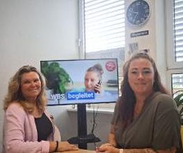 Beratungsteam mit viel Herz. 2 Frauen sitzen in einem Büro vor einem Bildschirm und blicken freundlich in die Kamera.