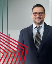 Der Geschäftsführer von actuell Personal steht in einem modernen Büro und lächelt freundlich in die Kamera. Mit Businesskleidung und professionellem Auftreten vermittelt das Bild Kompetenz, Vertrauen und Führungsstärke. Die Aufnahme unterstreicht die persönliche Betreuung, langjährige Erfahrung und die professionelle Unternehmenskultur von actuell Personal.