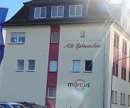 Mehrstöckiges Gebäude mit Firmenwerbung auf der Fassade. Davor stehen mehrere Autos.