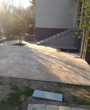 Neu gestaltete Terrasse mit Natursteinplatten aus Travertin und einer seitlichen Außentreppe am Wohnhaus. Die Arbeiten von Krippner, Garten- und Landschaftsbau bei Berlin verbinden eine großzügige Aufenthaltsfläche mit einem sicheren Zugang zum Gebäude.