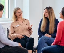Vier Personen sitzen in einem hellen Raum im Kreis und tauschen sich während eines gemeinsamen Gesprächs aus.