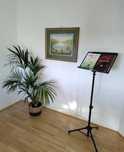 Ein Notenständer mit Lehr- und Übungsmaterial steht frei in einem hellen Raum.