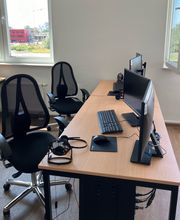 Moderner Arbeitsbereich ausgestattet mit 2 Bildschirmen, Tastatur, Maus und Headset sowie 2 schwarzen, komfortablen Bürostühlen. 