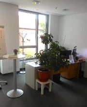 Ein Arbeitsplatz vor einer Fensterfront. Neben dem Tisch steht ein Flipchart mit der Aufschrift "Herzlich Willkommen!", auf der anderen Seite des Tisches steht ein beleuchtetes Aquarium.