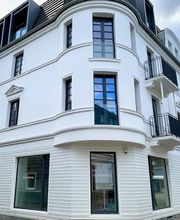 Außenansicht des weißen, klassisch-modernen Eckgebäudes mit schwarz gerahmten Fenstern.