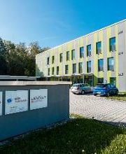 Außenansicht des Gebäudes an einem sonnigen Tag. Graue Fassade mit limonfarbenen Streifen. 