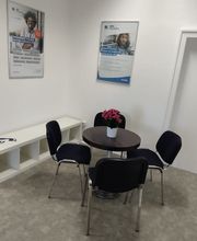 Sitzecke. Ein schwarzer Tisch mit Blumen und 4 Stühlen. Im Hintergrund hängen Poster an der Wand.