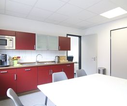 Eine rote Küche mit Mikrowelle, Kaffeemaschine, Wasserkocher und einer Vase mit Blumen. Weißer Tisch mit Stühlen.