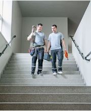 Auf dem Foto sind zwei Elektroinstallateur-Lehrlinge zu sehen, die eine elektrische Installation bei einem Gebäude verrichtet haben.