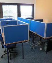 Schulungsraum mit 6 Arbeitsplätzen mit blauen Trennwänden. An der orangenen Wand hängt ein WBS TRAINING Plakat.