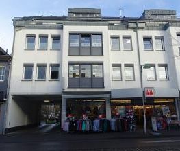 ein vierstöckiges, weißes Gebäude mit Ladenzeile im Erdgeschoss.