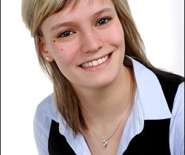 Portrait einer blonden Mitarbeiterin, die freundlich in die Kamera lächelt.