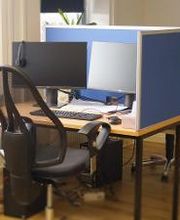 Typischer Teilnehmerarbeitsplatz mit einem schwarzen Bürostuhl und zwei Bildschirmen, Headset, Tastatur und Maus.