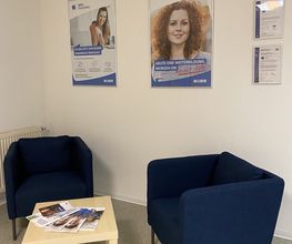Eine Sitzecke mit 2 Stühlen und einem kleinen Tisch. An der Wand 2 Plakate und 2 Zertifikate.