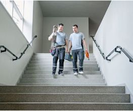 Auf dem Foto sind zwei Elektroinstallateur-Lehrlinge zu sehen, die eine elektrische Installation bei einem Gebäude verrichtet haben.