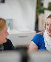 2 Frauen sitzen nebeneinander und schauen sich an.