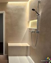 Sitzbank in der Dusche: Komfortable, geflieste Sitzgelegenheit in einer modernen, fugenlosen Dusche mit warmer Wandfarbe und dunkler Armatur.