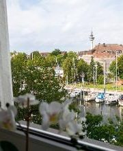 Blick aus dem Fenster am Standort. Ein Gewässer mit Segelbooten und vielen Bäumen.