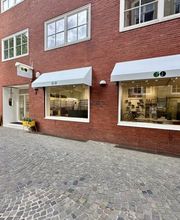 Newels Eyewear in Münster von außen mit großzügigen Schaufensterflächen und gut sichtbarem Firmenlogo. Durch die Fenster ist die moderne Präsentation der Brillen und Designerfassungen im Geschäft zu erkennen.