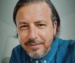 Portrait von einem Mitarbeiter mit grauen Haaren und Bart, der ein Jeanshemd trägt und freundlich in die Kamera schaut. 