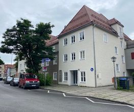 Außenansicht des Standorts Weilheim. Dreistöckiges Gebäude mit Spitzdach. Davor eine Einbahnstraße mit geparkten Autos.