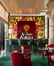 Vibrant cocktail bar at The Woodward Geneva with red velvet chairs, colorful glass accents, and lake views.