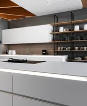 Moderne, grifflose Designküche mit großzügiger weißer Kücheninsel, integriertem Kochfeld und indirekter LED-Beleuchtung. Offene Holzregale mit schwarzem Metallrahmen, eine dunkle Rückwand und die sichtbare Holzbalkendecke schaffen einen eleganten Kontrast zwischen minimalistischem Küchendesign und natürlicher Architektur.