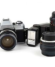 Display of camera and optical equipment including digital cameras, lenses, and photography accessories arranged on store shelves.