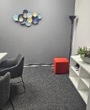 Arbeitsbereich mit 2 PC-Bildschirmen, Tastatur, Maus und Headset. Hellgraue Wände mit Dekoration. weißes Regal mit Topfpflanze.