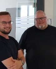 Zwei Männer mit schwarzen Shirts,. die in die Kamera schauen.