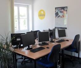 Schulungsraum mit 4 Arbeitsplätzen jeweils mit 2 Bildschirmen, einem Bürostuhl, Tastatur und Maus. An der Wand hängt ein Plakat.