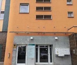 Außenansicht vom Gebäude der Einrichtung mit einer orangenen Fassade und mehreren Schildern sowie Briefkästen im Eingangsbereich.