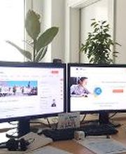 Arbeitsplatz mit 2 Bildschirmen, Tastatur, Maus und Headset. Dahinter mehrere Pflanzen.