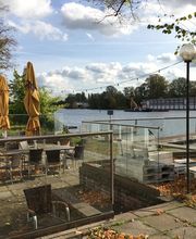 Bild von der Terrasse mit Sitzgelegenheiten und Sonnenschirmen. Daneben ein Gewässer.