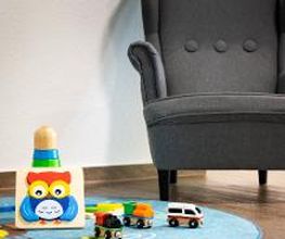 Kinderecke mit einem türkisen Teppich und Spielzeug. Dahinter ein grauer Kindersessel.