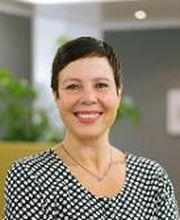 Frau mit kurzen dunklen Haaren und gepunkteter Bluse.