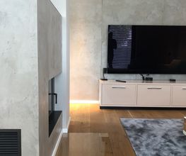 Exklusive Wohnraumgestaltung in handgearbeiteter Betonoptik mit integriertem Kamin, TV-Wand und indirekter Beleuchtung.