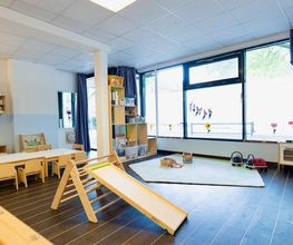 Heller Gruppenraum der Partou Kita Wandsbeker Chaussee mit Spielteppich, Pikler-Dreieck, Rutsche und vielfältigen Spielmaterialien