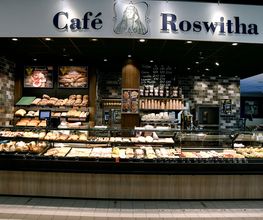 CAFÉ ROSWITHA
„Roswitha von Gandersheim“ durfte es am Ende nicht heißen, aber mit der knapperen Variante, „Café Roswitha“, erhalten wir auf eine liebevolle und persönliche Weise das Andenken an die erste Dichterin Deutschlands aufrecht. Wir laden dich ein, den Stress für die Dauer deines Aufenthaltes im Auto auf dem Parkplatz zurückzulassen und es dir in unserem „Café Roswitha“ im Vorkassenbereich gemütlich zu machen.

Mit dem großen, doppelten Sitzbereich von über 70 Sitzplätzen und einer Außenterrasse mit ca. 30 Sitzplätzen ist für jeden Gast genügend Freiraum garantiert. Bei kaltem Wetter lässt es sich im Innenbereich in der Kaminecke mit einer Tasse frisch gemahlenem Kaffee und einem Stück Kuchen oder Torte in den Sesseln vor dem Kamin wohlfühlen. Das Café ist schon frühmorgens unser „Hotspot“.