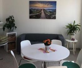 Aufenthaltsraum mit Sofa und Beistelltisch, auf dem Pflanzen stehen. Davor ein Tisch mit 5 Stühlen.