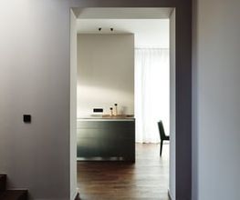 Reduziert, klar und atmosphärisch: Der Blick durch den Flur in den Wohnbereich offenbart ein Zusammenspiel aus hochwertigen Materialien, gedeckten Farben und architektonischer Präzision. Natürliches Licht und ausgewählte Details verleihen dem Raum Ruhe und Tiefe.