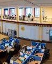 Fisheye-Aufnahme des Arbeitsbereichs und des Aufenthaltwsbereichs. Es befinden sich mehrere, abgetrennte PC-Arbeitsplätze vor Ort. Im Aufenthaltsbereich sieht man mehrere Sofas und Tische an einer Fensterfront.