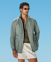 Mid green field jacket with raglan shoulders and a sleek hip-length cut. Features hidden snap buttons, zip closure, and an interior waist drawstring. Includes flapped and slanted pockets.