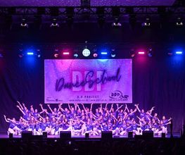 D.D.Project - Hip-Hop Tanzschule Dresden Große Tanzgruppe bei einer Bühnenaufführung mit farbiger Lichtshow und Publikum, ideal für Inhalte zu Tanzschule, Showdance und Bühnenperformance.