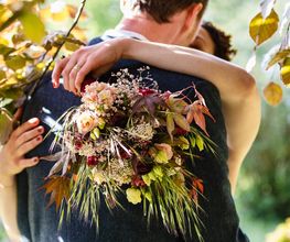 Hochzeitsfotograf Tom Maiwald - Emotionales Detail eines Brautpaares bei einer Umarmung mit herbstlichem Brautstrauß im Mittelpunkt. Natürliche Hochzeitsfotografie mit Fokus auf Blumen und persönliche Momente.