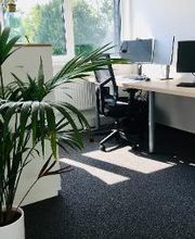Schreibtisch im Trainingsraum mit zwei Bildschirmen, Tastatur, Headset und Maus. Durch das Fenster strahlt viel Sonnenlicht herein.