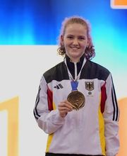 Eine Sportlerin steht auf einer Siegerbühne und hält eine Medaille in der Hand. Die Situation vermittelt Erfolg und einen offiziellen Wettbewerbsrahmen.