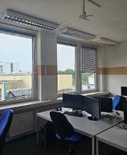 Schulungsraum mit mehreren Arbeitsbereichen, die mit 2 PC-Bildschirmen, Tastatur, Maus und Headset ausgestattet sind. Fensterreihe.