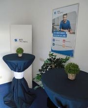 Beratungsbereich mit mehreren Bistrotischen, die mit blauen Hussen überzogen sind. Darauf stehen Tischpflanzen.